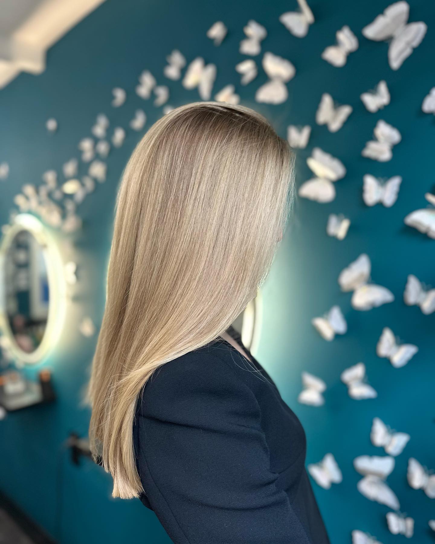 Cool blonde balayage in front of the butterfly wall